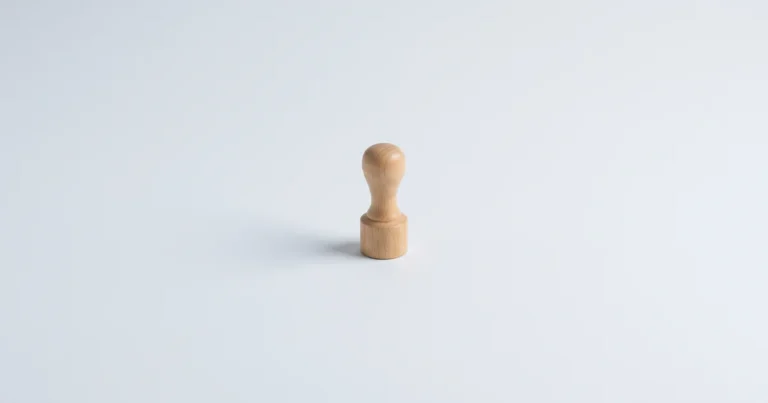밝은 회색 배경 위에 손잡이가 달린 둥근 나무 결재 도장 하나가 놓여 있다. 세금계산서를 발급하는 일을 상징한다.